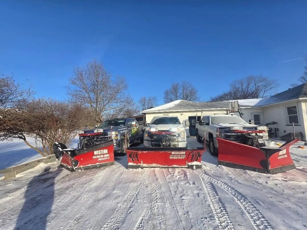 Three AAG pickup trucks fitted with red snow plows lined up in a snowy driveway